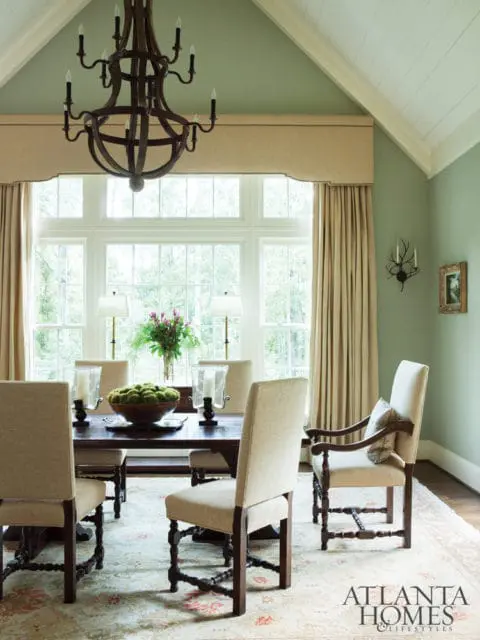 Dining room with a dark wood table and chairs upholstered in light beige fabric, a large multi-paned window, and a wrought iron chandelier.