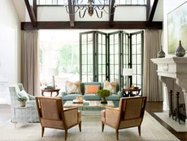 Living room with teal sofa, patterned armchairs, and stone fireplace. Large bi-fold doors open to an outdoor patio.