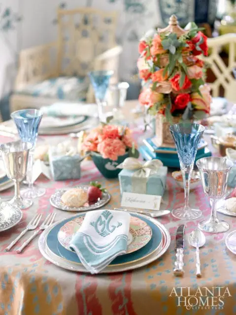 Table setting with blue glassware, silver goblets, floral centerpiece, and monogrammed napkins on a colorful ikat tablecloth.