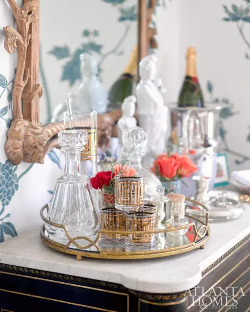 Bar cart with crystal decanters, gold-rimmed glasses, champagne bottles, and floral arrangements on a marble countertop.