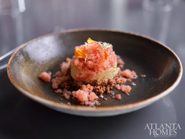 Dessert with pink sorbet, crumbled cookie base, and edible gold leaf, served in a dark, textured bowl with Atlanta Homes & Lifestyles logo in the corner.