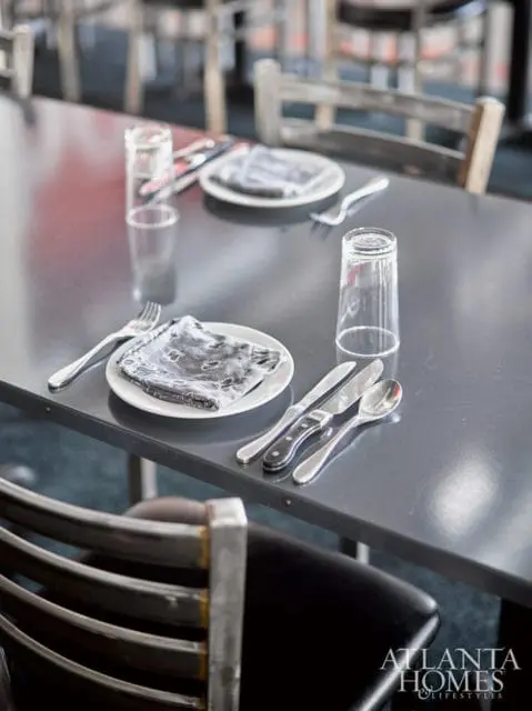 Dark gray table set with white plates, silverware, and clear glasses. Chairs with black upholstery and metal frames are visible.