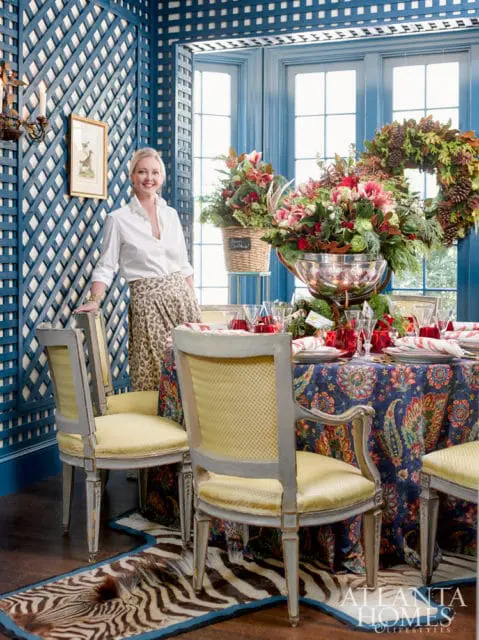Woman in white shirt and leopard print skirt standing by a dining table set for a holiday meal, with a blue lattice wall and floral tablecloth.