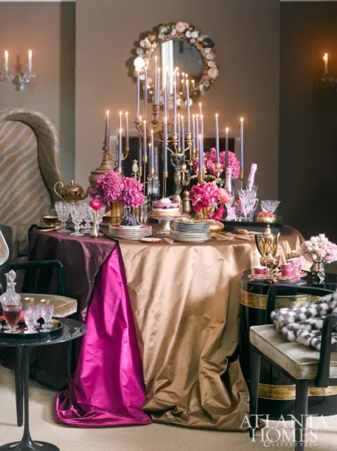 Dining table set with gold and plum tablecloths, pink hydrangeas, ornate candelabras with purple candles, and a cake. A decorative mirror hangs above.