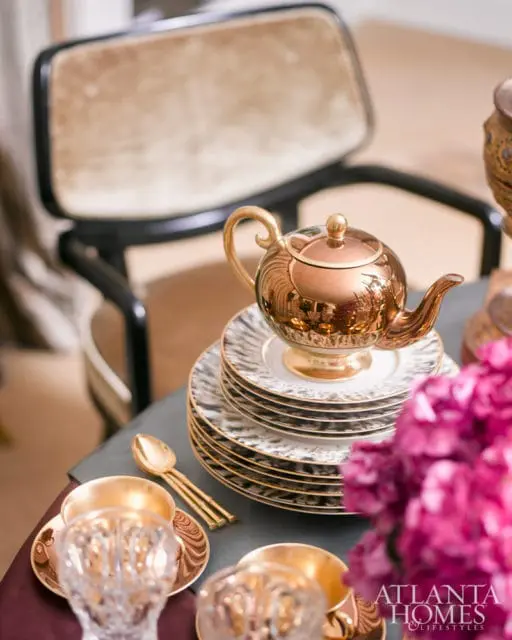 Stack of plates with gold trim and a copper teapot on top, with gold spoons and crystal cups