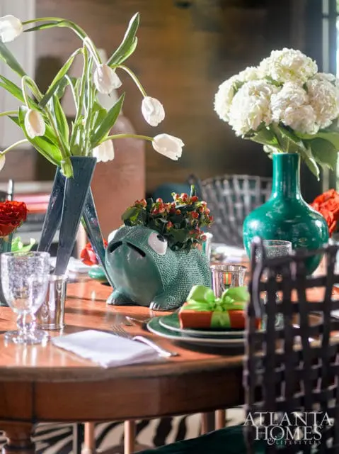 Wooden dining table set with white tulips, white hydrangeas, a frog planter, and a gift box tied with a green ribbon.