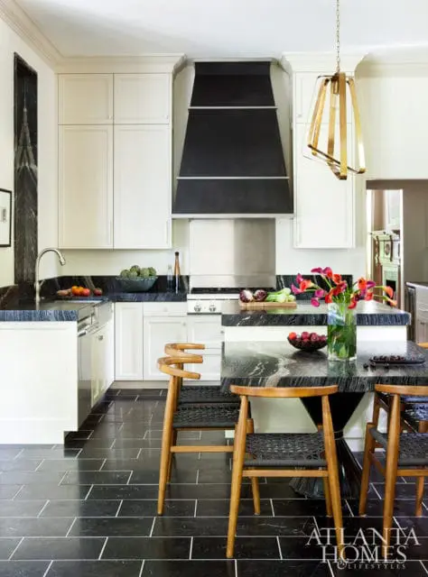 White kitchen with black marble countertops and island, black tile flooring, a black range hood, and a gold pendant light.