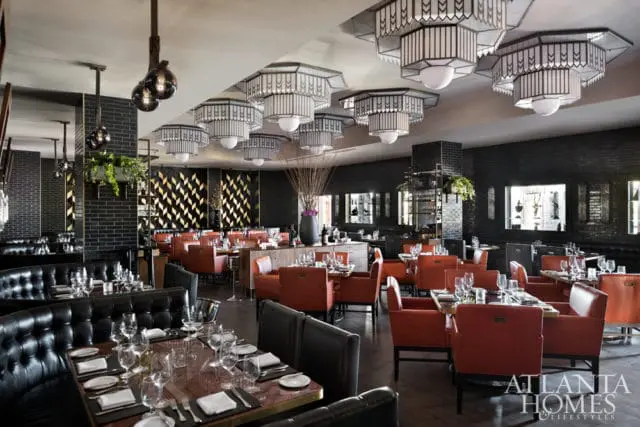 Restaurant dining room with black leather booths, orange leather chairs, dark brick walls, and ornate geometric chandeliers.