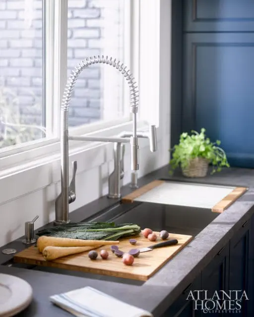 Kitchen sink area with a stainless steel faucet, cutting board with parsnips and radishes, and dark blue cabinetry.