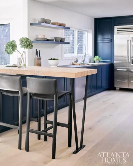 Navy blue kitchen cabinets with a light wood countertop island, black bar stools, and stainless steel appliances.