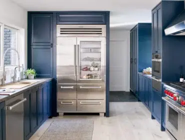 Navy blue kitchen with stainless steel Sub-Zero refrigerator, Wolf range with red knobs, and white subway tile backsplash.