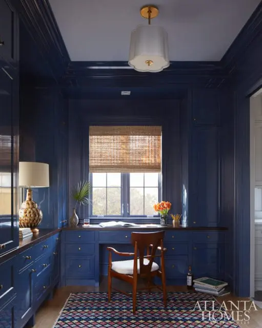 Dark blue lacquered built-in cabinetry and desk with a wooden chair and a woven window shade.