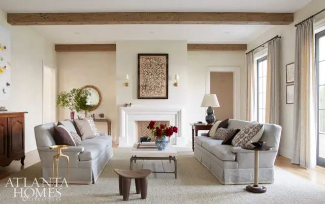 Living room with two light blue sofas, a white fireplace with abstract art above, and exposed wooden ceiling beams.