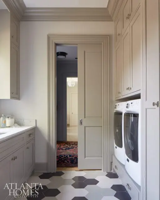 Laundry room with gray cabinetry, white washer and dryer, and hexagonal tile flooring. A doorway opens to a hallway with a Persian rug.
