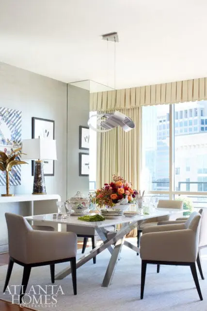 Dining room with a marble-top table, upholstered chairs, and a large window overlooking a city skyline. A floral centerpiece adorns the table.
