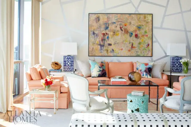 Living room with coral sofas, abstract art, geometric wall pattern, and ornate chairs.