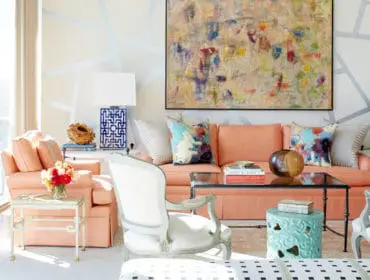 Living room with coral sofa, abstract art, white armchair, and blue patterned lamps. Geometric wall design in pale gray and cream.