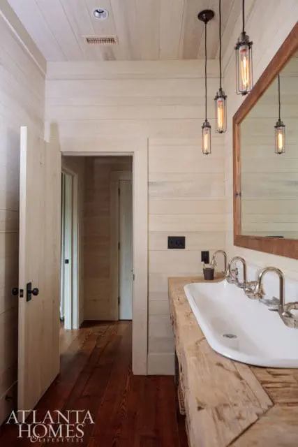 Bathroom with light wood plank walls and ceiling, dark wood floors, a double sink with a rough-hewn wood vanity, and industrial pendant lights.