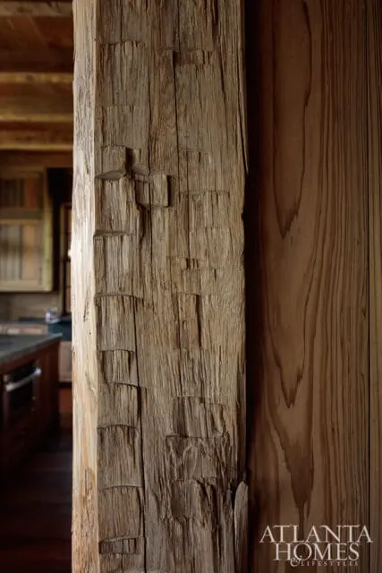 Close-up of a rough-hewn wooden beam with carved indentations, next to a smooth wooden wall.