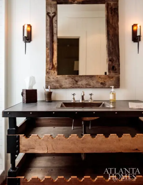 Rustic bathroom vanity with a metal countertop, undermount sink, and open wooden shelving. A reclaimed wood mirror hangs above, flanked by sconces.