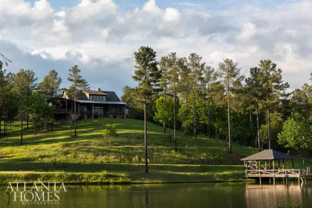 Log cabin-style house on a grassy hill overlooking a lake, with a wooden gazebo and dock on the right