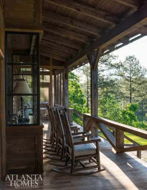 Wooden porch with rocking chairs and a view of trees. The porch has a rustic design with exposed wooden beams and a wooden railing.
