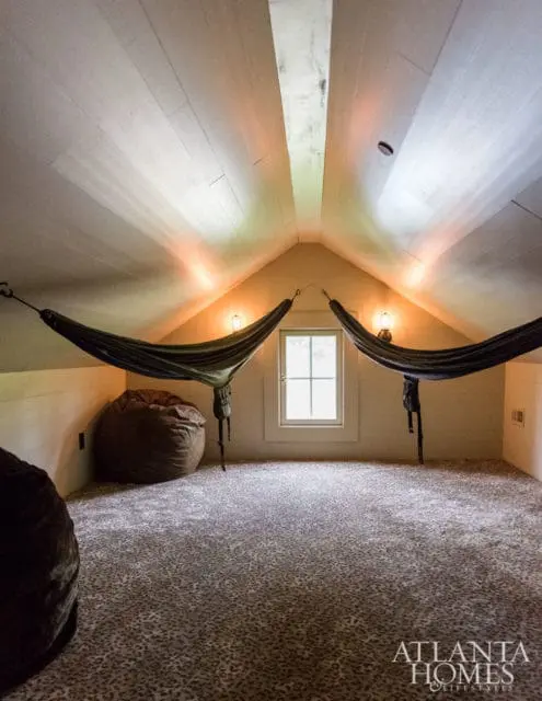 Attic room with sloped ceiling, two dark green hammocks, a large brown beanbag chair, and leopard-print carpet. A small window is centered on the back wall.