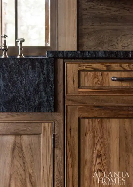 Kitchen detail featuring a dark veined stone countertop and backsplash, brass faucets, and warm wood cabinetry with visible grain.