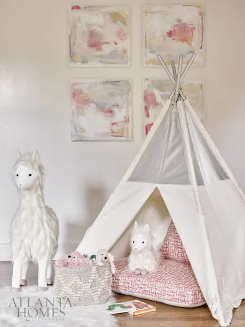 Child's play area with a white teepee, plush llama toys, a woven basket of stuffed animals, and abstract art on the wall.