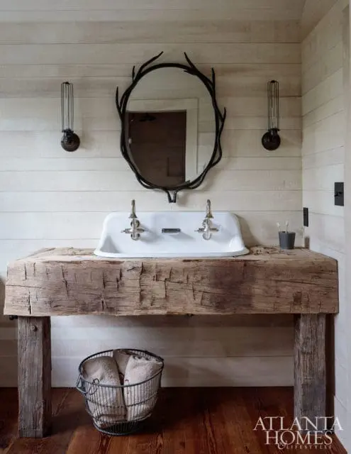 Rustic bathroom with a white vessel sink atop a reclaimed wood vanity, a twig-frame mirror, and plank walls.