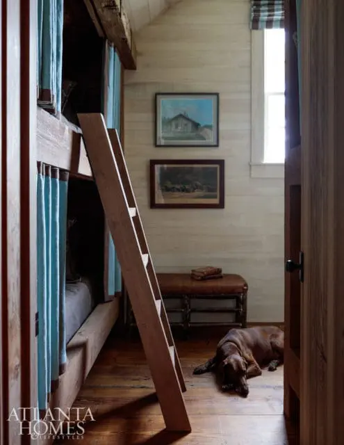 Rustic bedroom with wooden bunk beds, light wood paneled walls, a leather bench, and a brown dog lying on the floor.