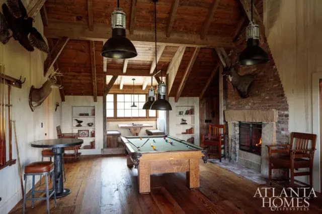 Rustic game room with pool table, fireplace, taxidermy mounts, and exposed wooden beams.