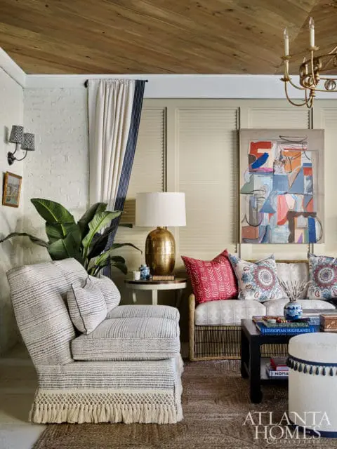 Living room with a textured armchair, a sofa with patterned pillows, a dark coffee table, and abstract art on the wall.