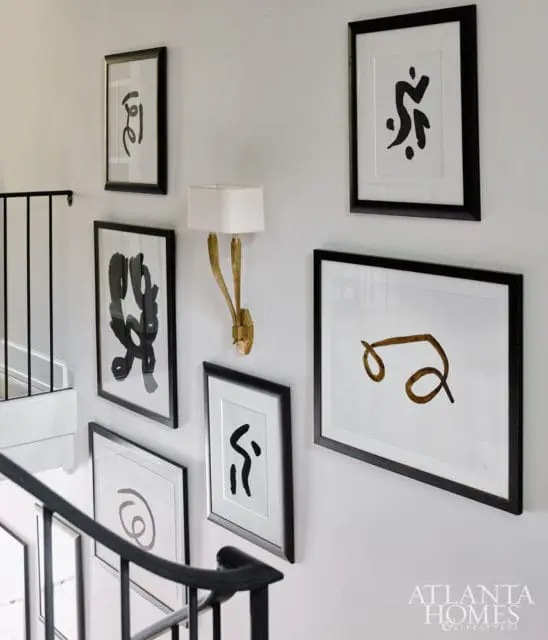 Hallway with a black metal banister, a gold sconce, and a gallery wall of framed abstract art in black and white.