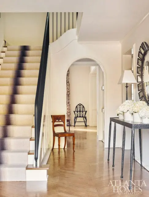Hallway with a carpeted staircase featuring a dark banister, a wooden chair, and an arched doorway leading to another room with a decorative chair.