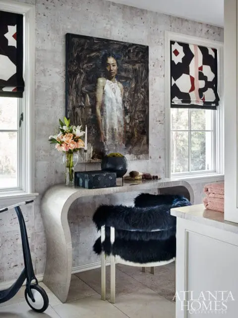 Interior room with textured wallpaper, a painting of a woman, a curved console table with decorative items, and a black faux fur chair.
