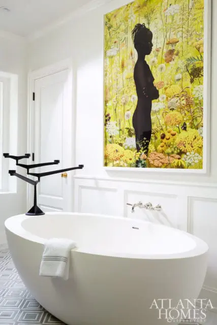 White bathroom with freestanding oval tub, black sculptural faucet, and large framed artwork of a silhouette against a yellow floral background.