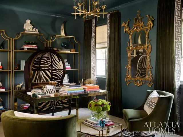 Dark teal office with gold shelving, a zebra print chair, a gold ornate mirror, and a brass desk