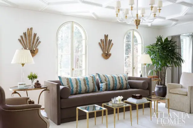Living room with a brown sofa adorned with blue and white striped pillows, flanked by arched windows and ornate wall sconces.