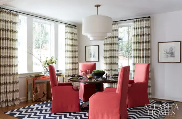 Dining room with coral upholstered chairs around a dark wood table, patterned curtains, and a black and white chevron rug.
