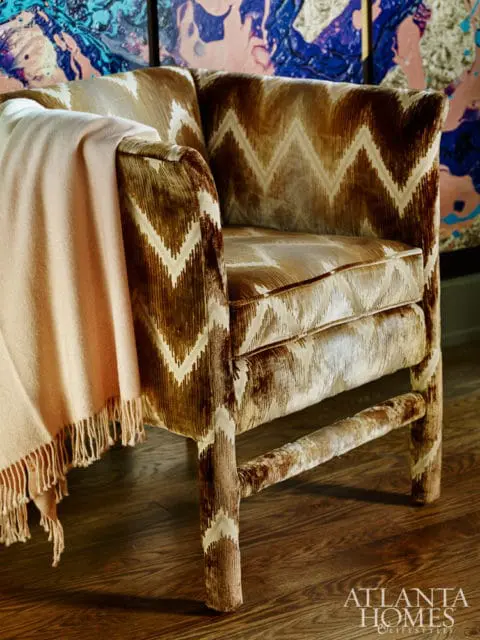Armchair upholstered in brown and cream ikat fabric with a light pink throw blanket draped over the arm, set on a dark wood floor.