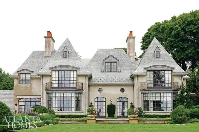 French-inspired mansion with grey slate roof, stucco facade, multiple gabled dormers, and large grid windows.
