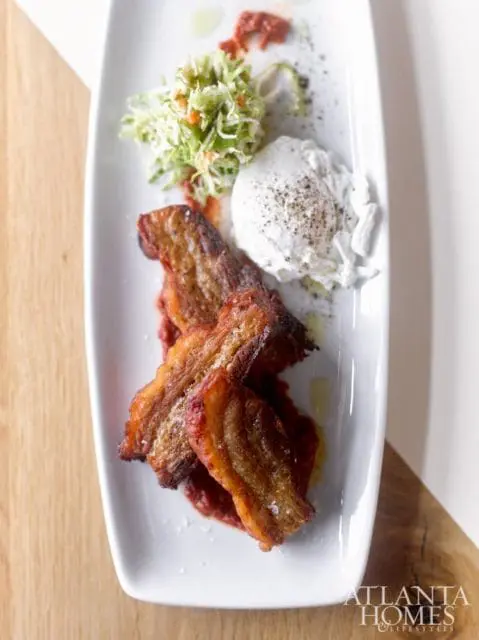 Crispy pork belly served with a dollop of white cheese, a side of coleslaw, and a smear of red sauce on a white platter.