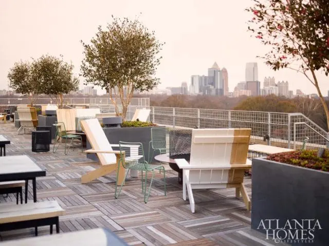 Rooftop patio with wooden deck, modern chairs, planters, and a city skyline in the background.