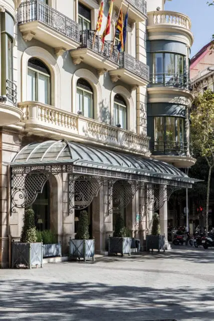 Ornate glass and metal awning over the entrance of a light-colored building with arched windows, balconies, and flags.