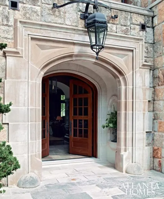 Stone mansion entrance with arched wooden double doors, ornate lantern, and decorative stone trim.