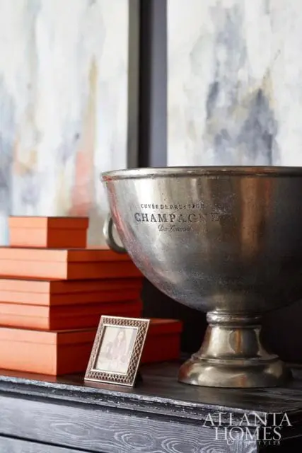 Silver champagne bucket with 'CUVEE DE PRESTIGE CHAMPAGNE Du Louvois' engraving, stacked orange boxes, and a small framed photo on a dark wood surface.
