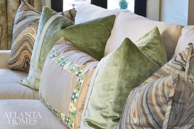 Living room with a sofa adorned with an assortment of decorative pillows in various textures and patterns, including green velvet, taupe with geometric trim, and marbled designs.
