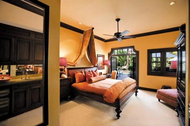 Bedroom with orange walls, dark wood trim, a dark wood four-poster bed with orange bedding, and French doors opening to a pool area.