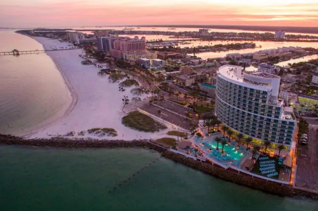 Aerial view of Opal Sands Resort at sunset, featuring a curved modern building, swimming pools, beach, and oceanfront cityscape.